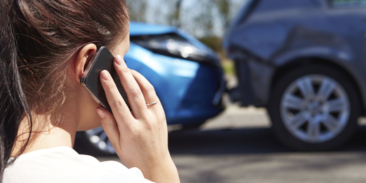 woman with mobile in front of a car crash