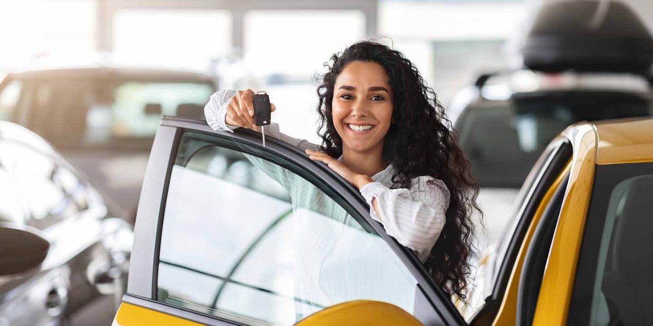 Young woman smiling and receiving keys to a new car 