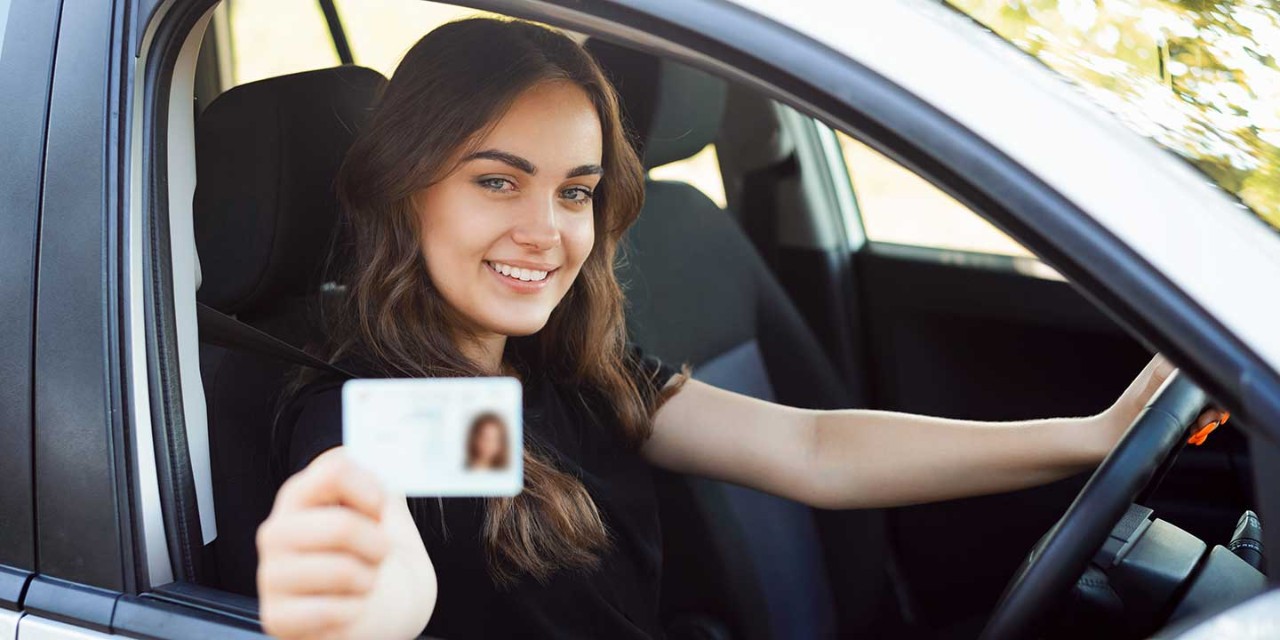 Happy driver sitting in the modern silver car and showing driving car license