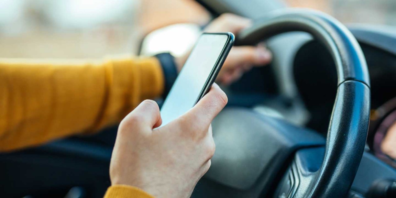 hand on steering wheel using phone to search direction