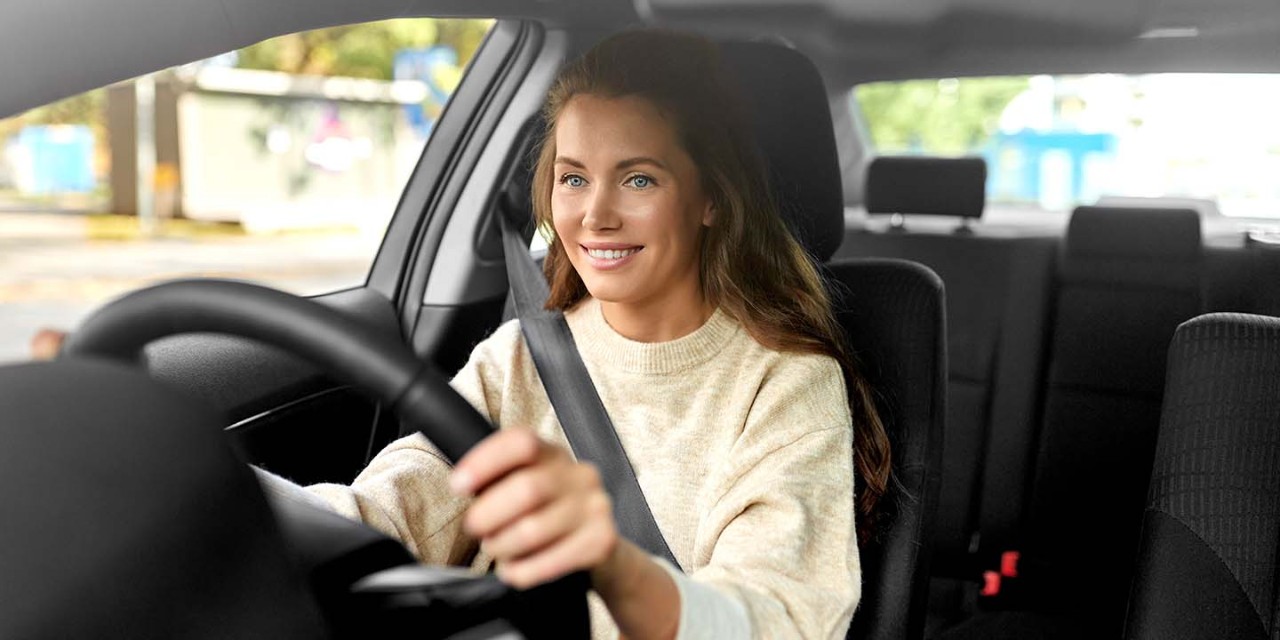 Smiling young woman holding steering wheel while driving car