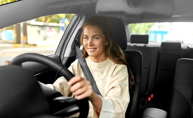 Smiling young woman holding steering wheel while driving car