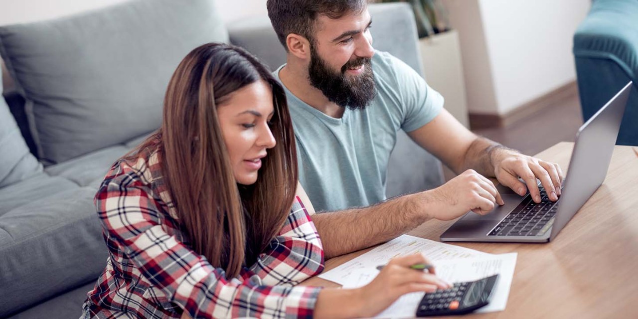 couple sitting in the living room using calculator and laptop