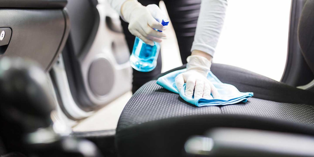 Close up of female wearing gloves while cleaning car interior with disinfection liquid sprayer and microfiber cloth.