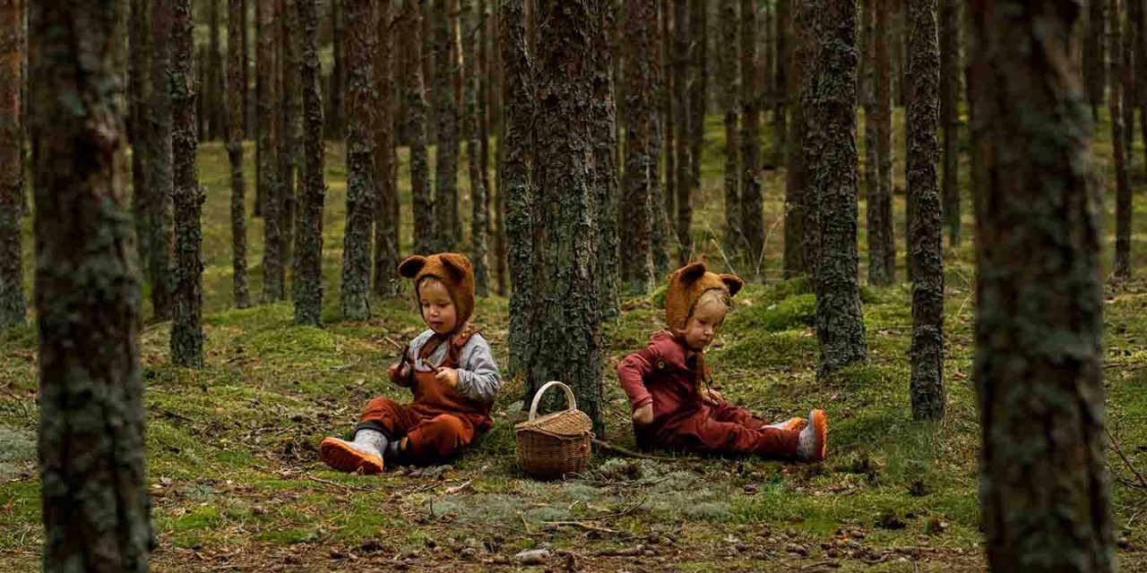 Two boys dressed up as bears in a forest sitting down