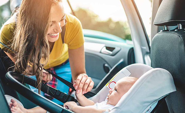 Young mother putting her baby boy on a safety child car seat.