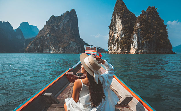 Young woman wearing boho hat and sittingin a boat on the lake with a spectacular mountain and lake view