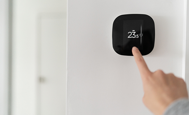 Cropped view on woman hand press button and adjusting temperature at home on room thermostat which hanging on white wall.