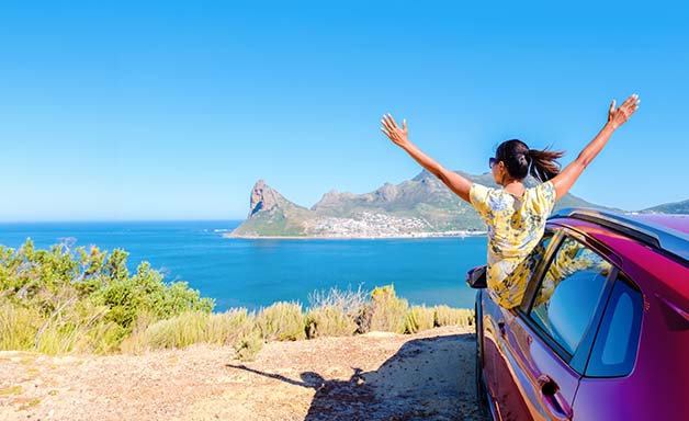 Car road trip travel fun happy woman tourist with open arms at ocean view from car driving on beach